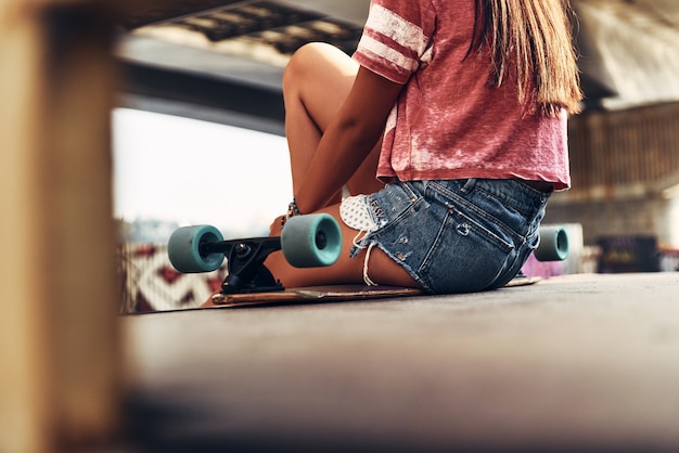 Gewoon uitrusten. Close-up achteraanzicht van een jonge vrouw die op het skateboard zit terwijl ze buiten tijd doorbrengt in het skatepark