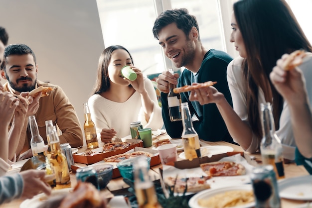 Gewoon uitrusten. groep jongeren in vrijetijdskleding die pizza eet en glimlacht terwijl ze binnen een etentje hebben