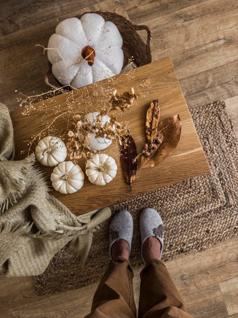 Gezellig herfsthuisinterieur Damesvoeten in vilten pantoffels en corduroy broek naast een eiken bank met herfstdecor