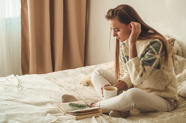 Gezellig huis. De mooie vrouw leest een boek op het bed. Goedemorgen met thee en boek. Vrij het jonge vrouw ontspannen. Het concept van lezen