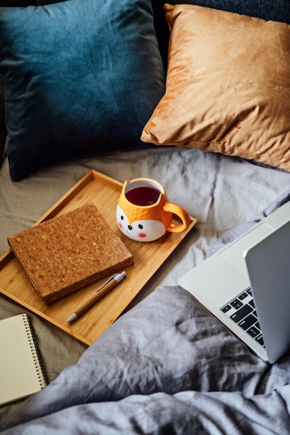 Gezellig huis herfst warme stemming laptop notebook en kopje thee op dienblad op deken in bed in het interieur