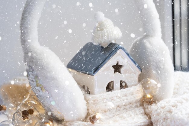 Gezellig huis is gewikkeld in een muts en sjaal in een sneeuwstorm vensterbank decor Wintersneeuw huisisolatie bescherming tegen kou en slecht weer kamerverwarming Feeststemming Kerst Nieuwjaar