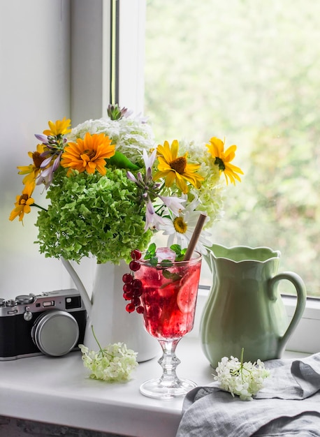 Gezellig huis stilleven boeket bloemen glas limonade kruik vintage camera op het raam in een lichte kamer