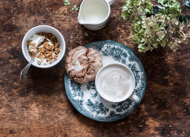 Gezellig huisgemaakt ontbijt Griekse yoghurt met granola chocolade meringue cappuccino op een houten tafelblad uitzicht