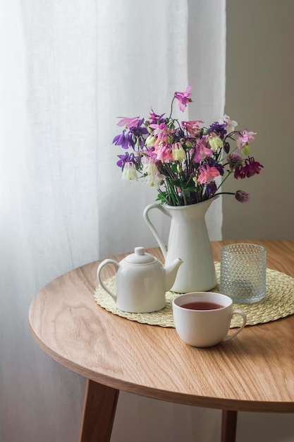 Gezellig keukeninterieur een kruik met zomertuinbloemen een kopje thee een theepot op een ronde houten tafel
