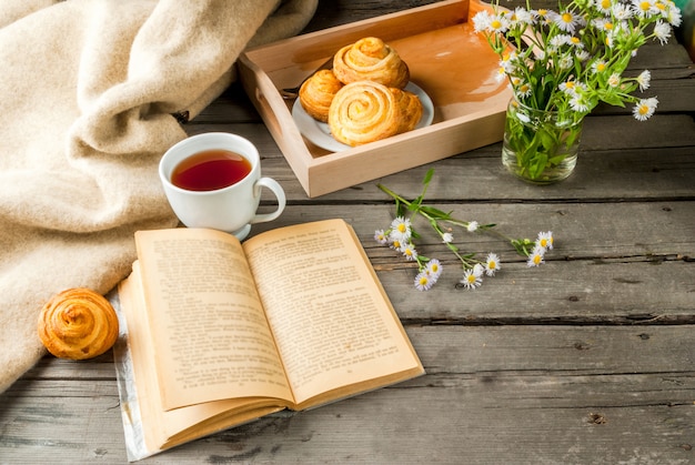 Gezellig ontbijt in de lente of vroege herfst thee, vers gebakken scones en een boeket veldmadeliefjes en een fascinerend boek. Kopieer ruimte