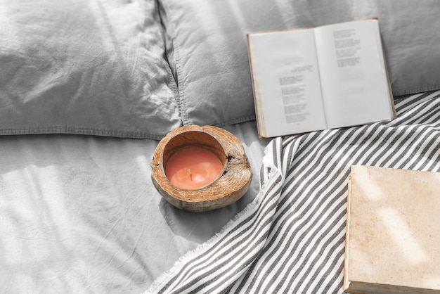 Gezellig rommelig bed met twee kussens, grijs beddengoed met boeken en kokosnootkaars.