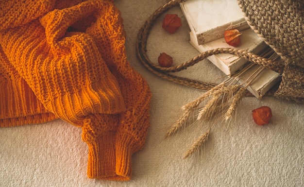 Gezellige gebreide warme oranje trui met oude boeken en vintage strozak op witte warme plaid met pompoen, physalis, herfstboeken en lezen. herfststemming. Herfst Wintertijd.