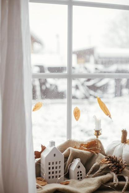 Gezellige herfst Stijlvolle pompoenkussens vallen bladeren kaarslicht en schattige gebouwen decoratie op bruine sjaal op vensterbank Herfst hygge herfst interieur Happy Thanksgiving