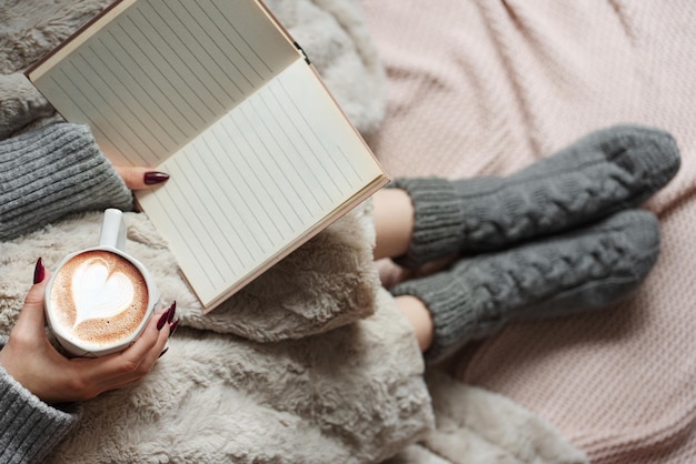 Gezellige huisvrouw bedekt met warme deken drinkt koffie en riet het boek