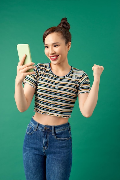 Gezellige mooie vrouw met Aziatische verschijning die selfie neemt of spreekt op videogesprek met behulp van mobiele telefoon geïsoleerd op groene achtergrond