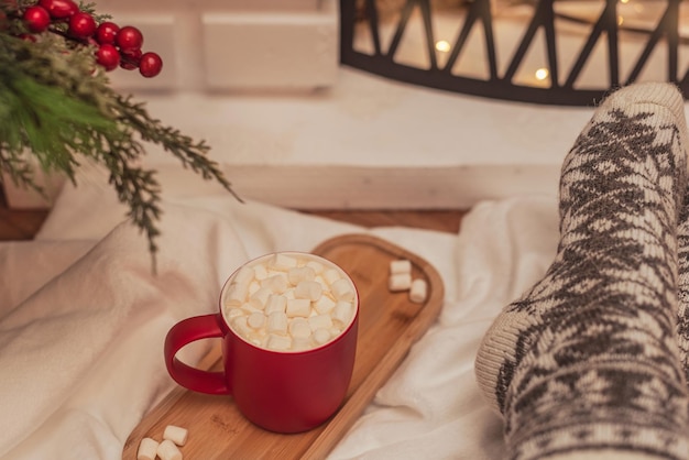 Gezellige sfeerscène met een kopje warme drank met witte marshmallows en vrouwelijke voeten in warme wollen sokken voor de open haard Selectieve aandacht Gezellige sfeer tijdens het concept van de wintervakantie