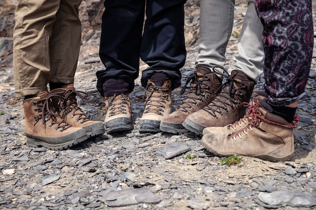 Gezelschap van toeristenbenen samen in bruine trekking wandelschoenen met veters op rotsachtige klif