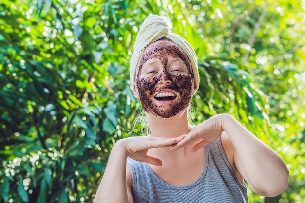 Gezicht Huid Scrub. Portret van sexy glimlachend vrouwelijk model dat natuurlijk koffiemasker, gezichtsscrub op de gezichtshuid toepast. Close-up van mooie gelukkige vrouw met gezicht bedekt met schoonheidsproduct. Hoge resolutie.