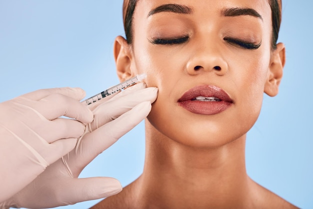 Gezicht injectie en schoonheid vrouw en cosmetische chirurgie en dermatologie geïsoleerd op blauwe achtergrond Antiaging huidverzorging en spuit vrouwelijk model en dokter handen met vloeibare collageen in de studio