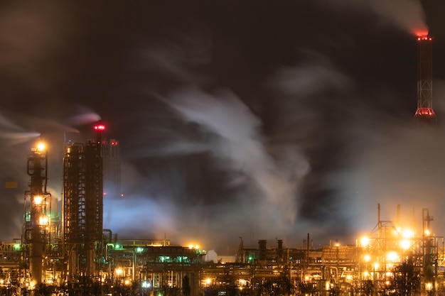 Gezicht op een grote fabriek of fabriek in het licht van nachtverlichting Er komt veel rook uit de schoorstenen van de fabriek Milieuvervuiling brand bij een afvalrecyclingfabriek