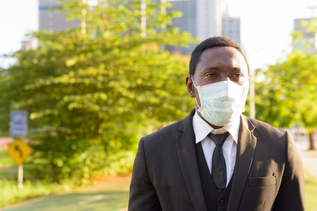 Gezicht van afrikaanse zakenman met masker denken in het park in de stad