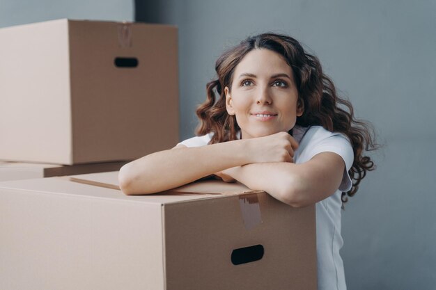 Gezicht van een jonge spaanse dame die droomt terwijl ze op de vloer zit in een nieuw appartement of huis