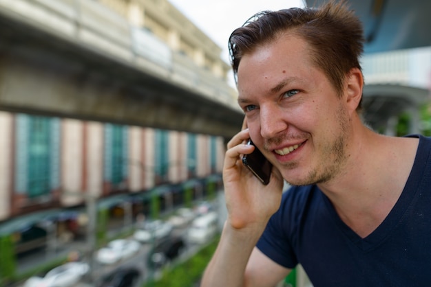 Gezicht van gelukkige jonge knappe man praten aan de telefoon op sky train station