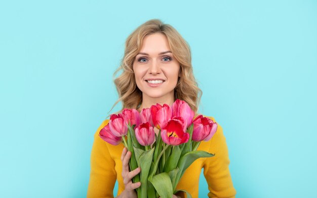 Gezicht van gelukkige jonge vrouw met lente tulp bloemen op blauwe achtergrond