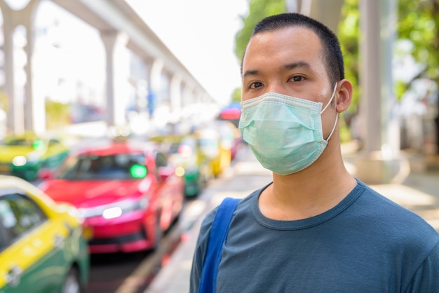 Gezicht van jonge Aziatische man met masker voor bescherming tegen uitbraak van coronavirus bij het taxistation in de stad