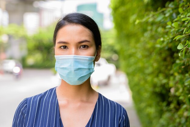 Gezicht van jonge Aziatische zakenvrouw met masker voor bescherming tegen uitbraak van het coronavirus in de straten buitenshuis