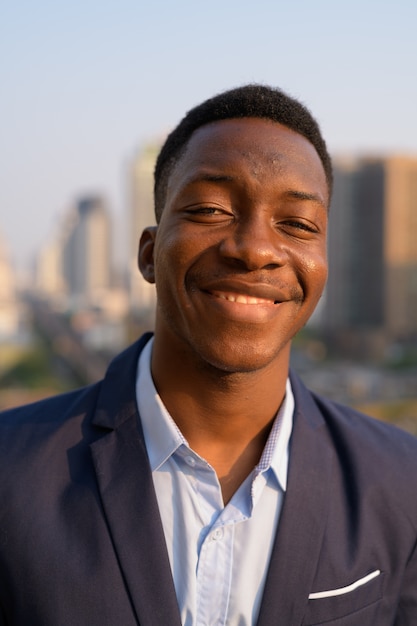 Gezicht van jonge gelukkig Afrikaanse zakenman lachend tegen uitzicht over de stad