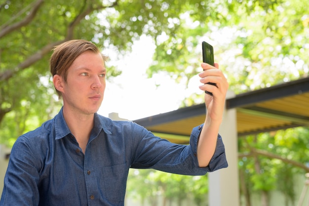 Gezicht van jonge knappe blonde zakenman selfie te nemen in het park buitenshuis