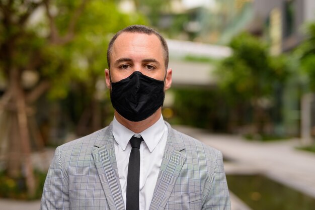 Gezicht van spaanse kale zakenman die masker draagt voor bescherming tegen de uitbraak van het coronavirus in de stad met de natuur