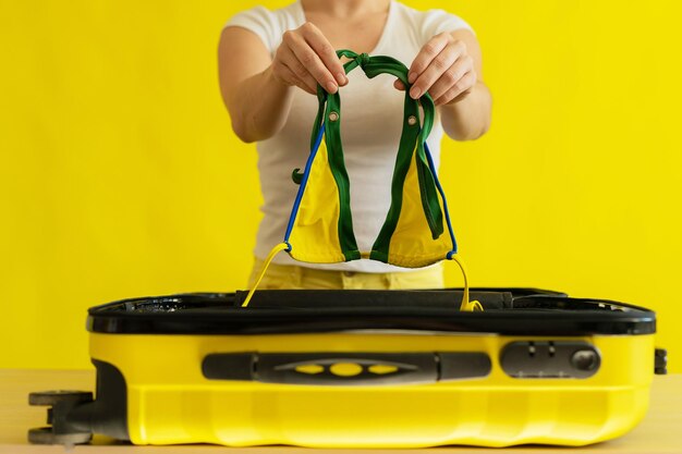 Gezichtloze vrouw verpakt een mini-bikini in een koffer op een gele achtergrond Het meisje gaat op reis naar de zee en stopt een zwembroek in een tas Klaar voor vakantie