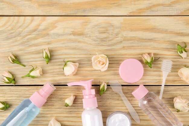 Gezichts- en lichaamscosmetica in roze flessen met verse rozen op een natuurlijke houten ondergrond. crèmes en lotions. spa. bovenaanzicht. ruimte voor uw tekst
