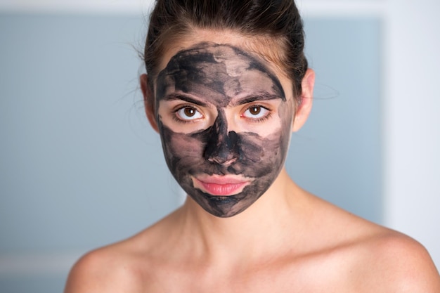 Gezichtsbehandeling mooie jonge vrouw met houtskool modder gezichtsmasker op gezicht huidverzorging en behandeling