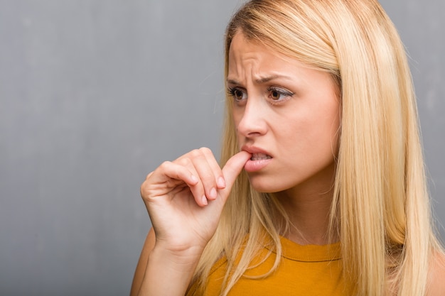 Gezichtsclose-up, portret van een natuurlijke jonge blonde vrouw het bijten spijkers