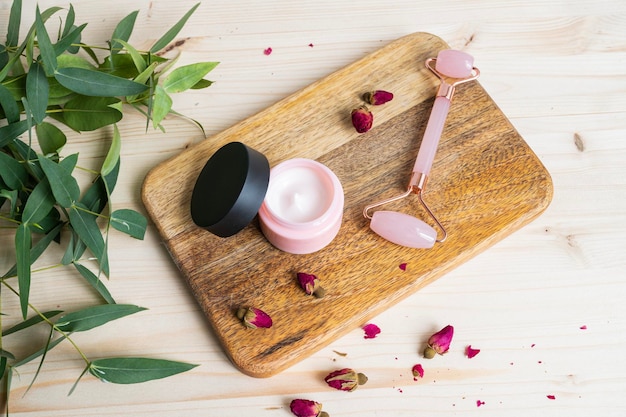 Gezichtscrème en stimulator op een houten tafel Het concept van zorgcosmetica met roos en eucalyptus Gezondheid en schoonheid