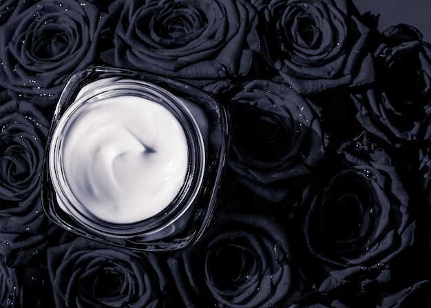 Gezichtscrème huid moisturizer en zwarte rozen bloemen luxe huidverzorging cosmetisch product op florale achtergrond als beauty merk vakantie flatlay design