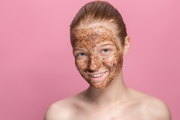 Gezichtshuid scrub koffiedik masker op het gezicht van een mooie jonge vrouw