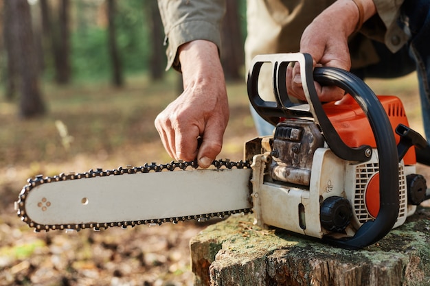 Foto gezichtsloze logger die de kettingzaag voorbereidt op het werk