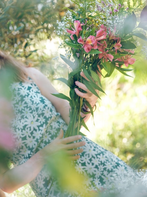 Gezichtsloze onherkenbare vrouw in een jurk met een creatief boeket verse bloemen terwijl ze in een groene tuin staat bij daglicht