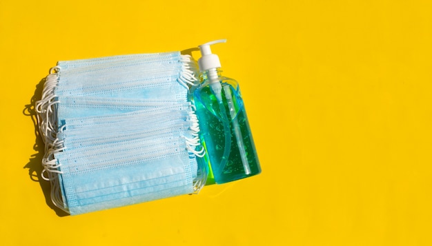 Gezichtsmaskers met alcohol vloeibaar gel-ontsmettingsmiddel op geel oppervlak
