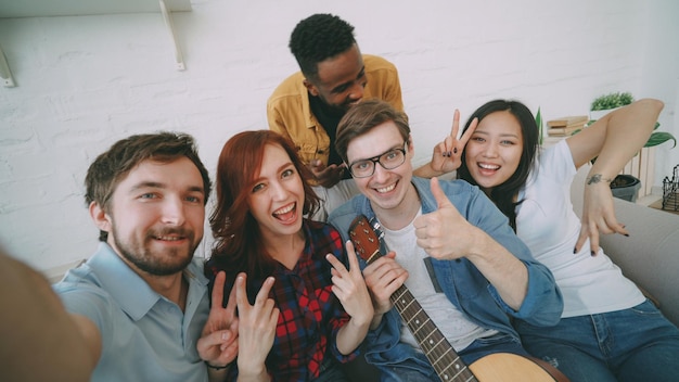 Gezichtspunt shot van multi-etnische groep vrolijke vrienden die selfie-foto's maken op smartphonecamera terwijl ze thuis feesten op een feestje