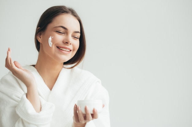 Gezichtsroomvrouw die crean op huid natuurlijk portret toepast. Studio opname.