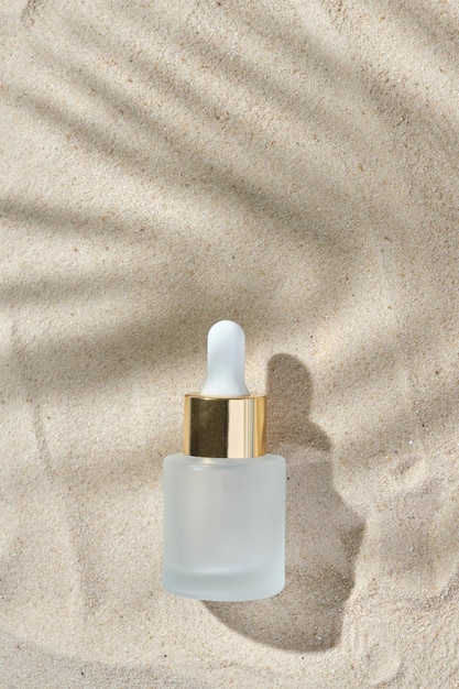 Gezichtsserum van glazen fles met een pipet op een natuurlijke achtergrond met zand Etherische olie voor het hydrateren van de lichaamshuid mockup van schoonheidsmode cosmetisch flesdruppelproduct met huidverzorgingsconcept