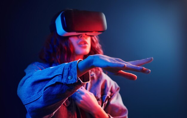 Gezichtsuitdrukking van een jong meisje met een virtual reality-bril op het hoofd in rood en blauw neon in studio