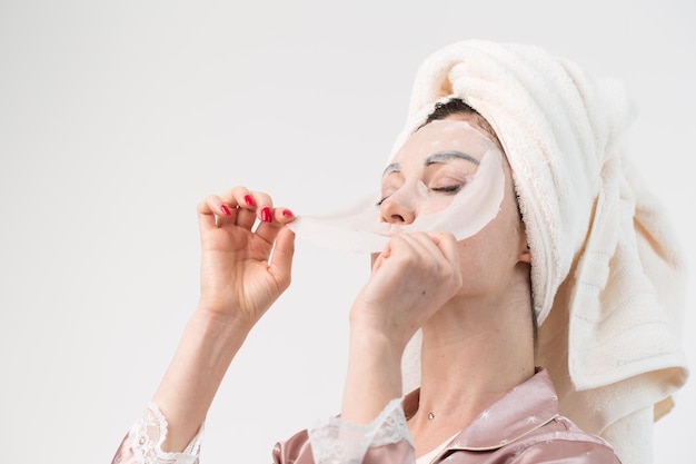 Gezichtsverzorging en schoonheidsbehandelingen Vrouw met een vel hydraterend masker op haar gezicht geïsoleerd op een witte achtergrond