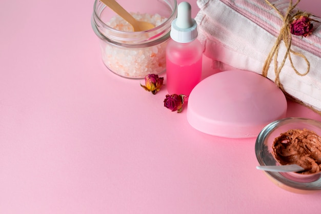 Gezichtsverzorgingcosmetica met organische scrub, masker, zeep en rozenolie op roze achtergrond met een handdoek