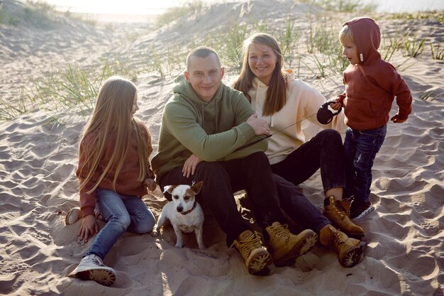 Foto gezin met een zoon en dochter en een hond zitten in de herfst op het zand
