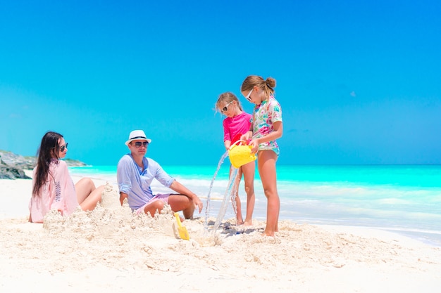 Gezin met twee kinderen maken zandkasteel op tropisch strand