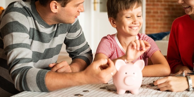 Gezinsbesparing met een spaarvarken Glimlachend kind met ouders die munten tellen Financiële planning Sparen van geld en familiebonding rond een spaarvak Ouders die hun zoon leren sparen