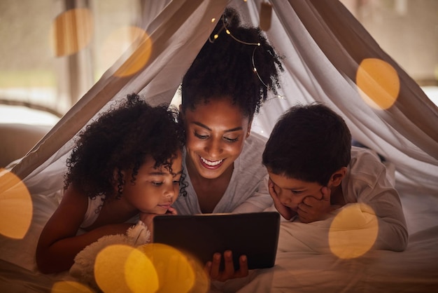 Gezinskinderen en tablet met een moedermeisje en jongen die thuis kamperen onder een deken in de slaapkamer Internet lezen en kinderen met een vrouw haar zoon en dochter die samen in hun huis een band vormen