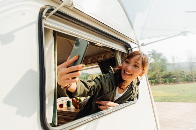 Gezinsreis met caravan op prachtige vakantie. Jonge Aziatische vrouw selfie met smartphone in caravan met witte koffiekop in de ochtend